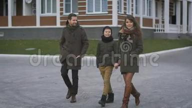 幸福的年轻家庭穿着温暖的衣服，一起走在街上笑着说话。 父亲和母亲